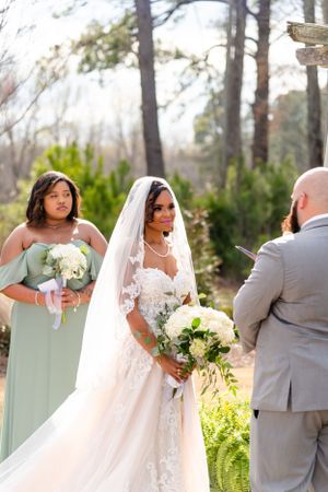 Outdoor wedding ceremony with bride in white gown and bridesmaid in sage green dress.