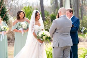 Beautiful outdoor wedding ceremony with bridal party in mint green and navy attire surrounded by greenery.