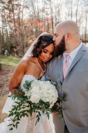 Intimate wedding portrait shows couple embracing with white roses and greenery bouquet.