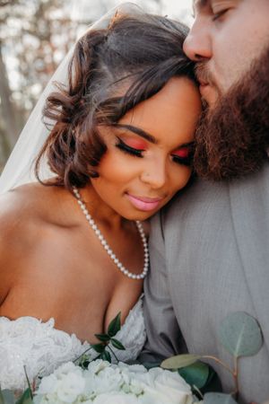Close-up of tender wedding moment with pearl necklace and white rose bouquet.