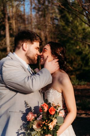 Tender moment between newlyweds with coral and peach bouquet in afternoon light.