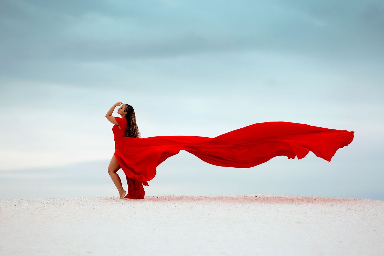 A flowing red dress billows dramatically in the wind against a minimalist white and blue background.