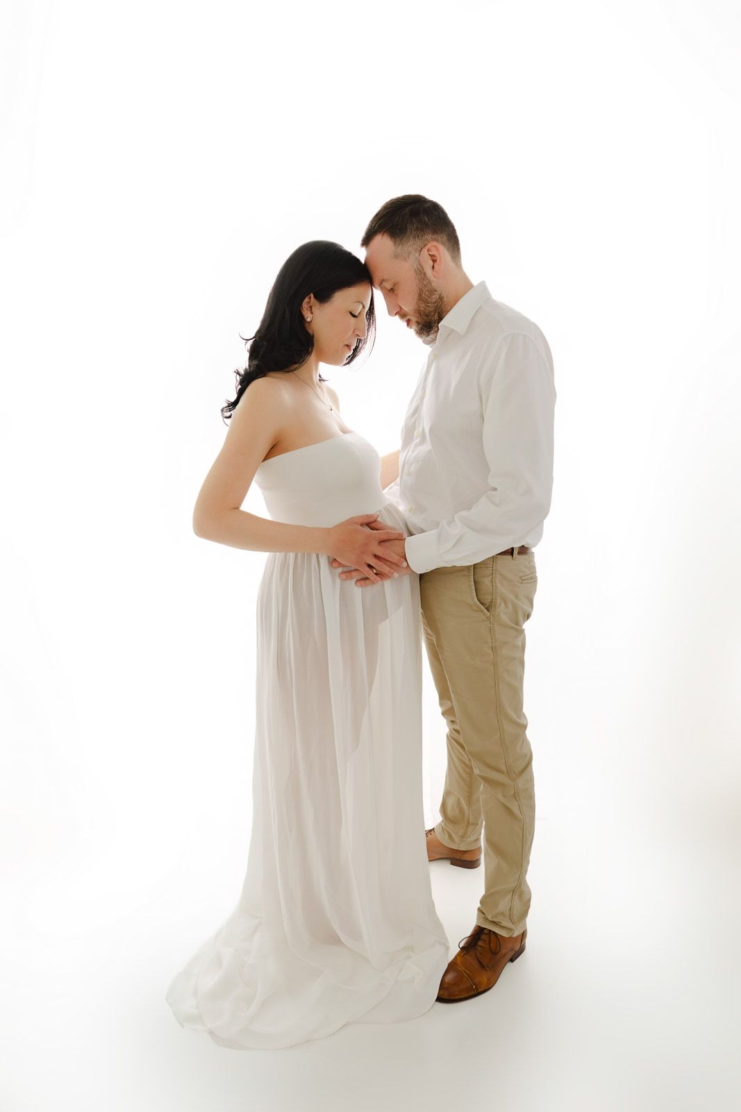 Expectant mother in a bright red sweater poses against white wall highlighting her pregnant belly.