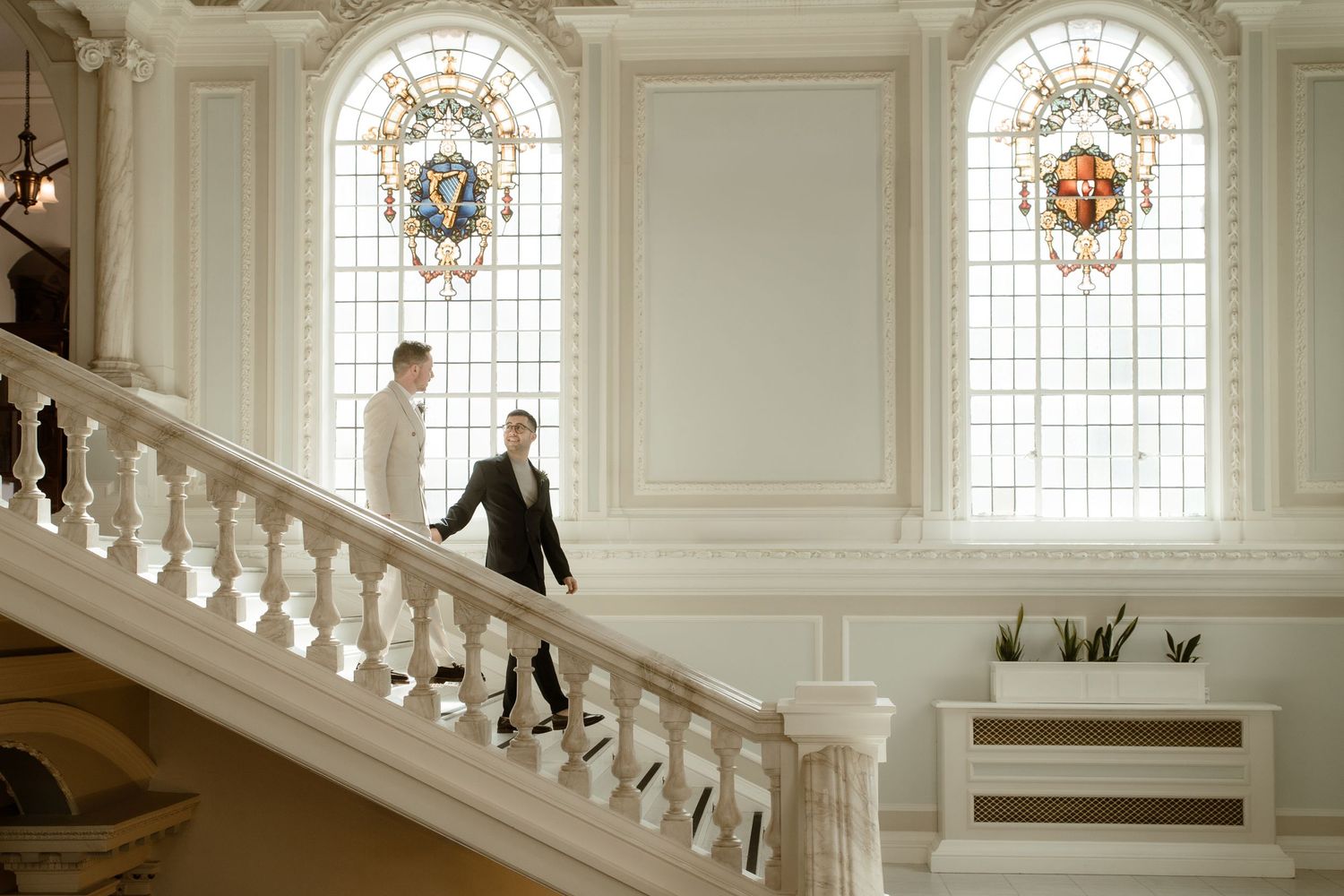 Elegant white staircase with ornate details and stained glass windows in a grand venue.