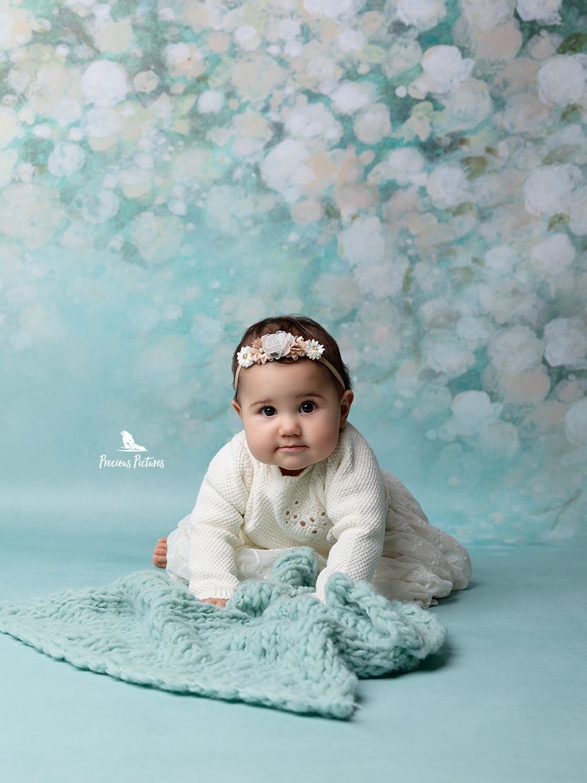 Beautiful baby girl in a white knit sweater and floral headband during a professional sitter session at Precious Pictures, Malta.