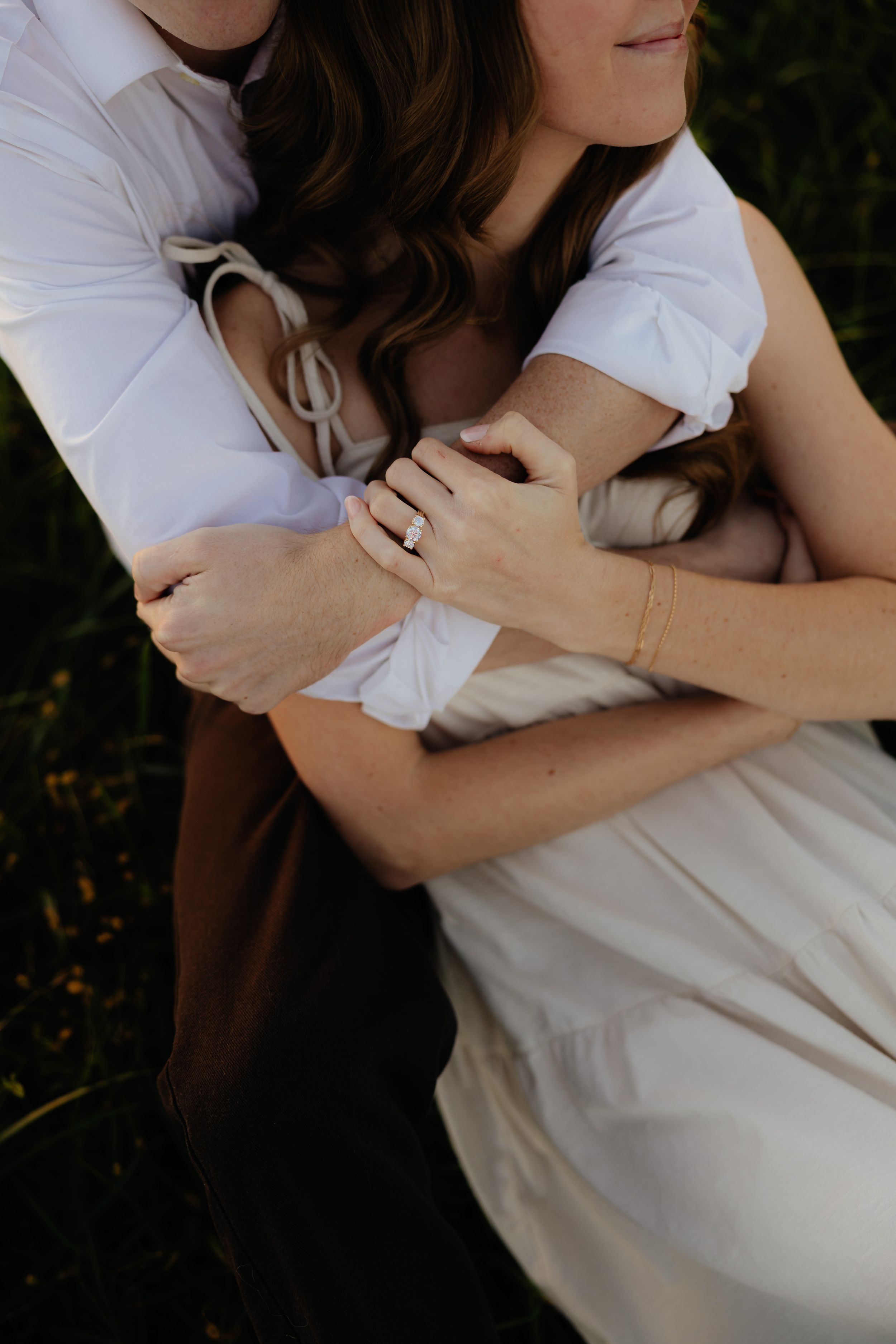 Close-up of couple embracing showing engagement ring and white clothing.