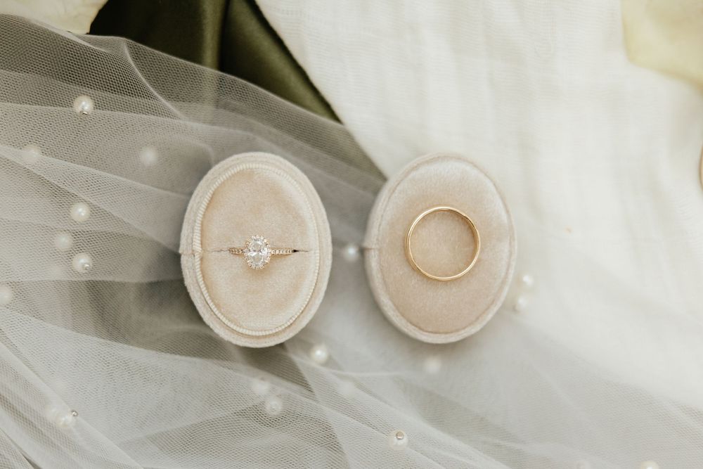 Delicate wedding rings rest on a textured surface in soft lighting.
