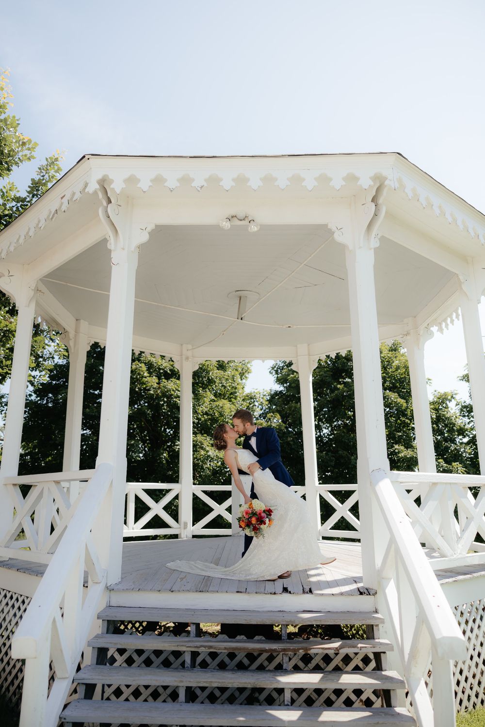 White wedding gazebo with ornate pillars and lattice details set against a bright summer sky.
