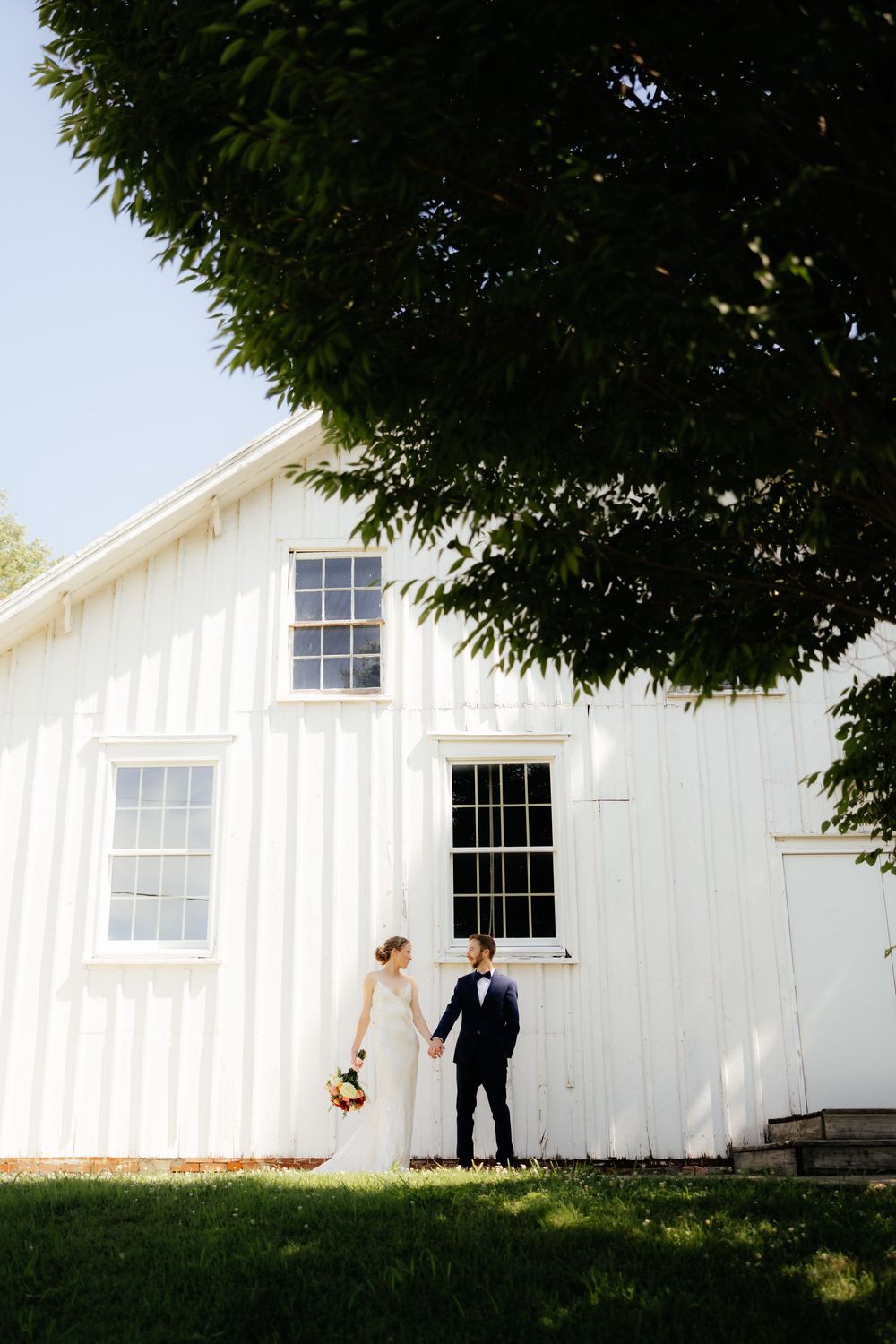 Wedding couple poses against a white barn building in dramatic silhouette.