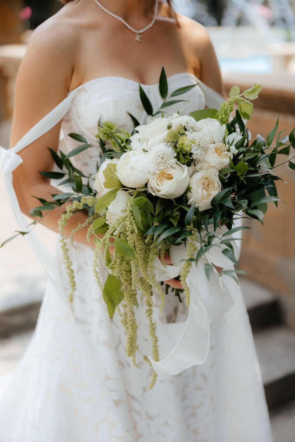 Elegant bridal bouquet with white roses, greenery and cascading elements against a white wedding dress.