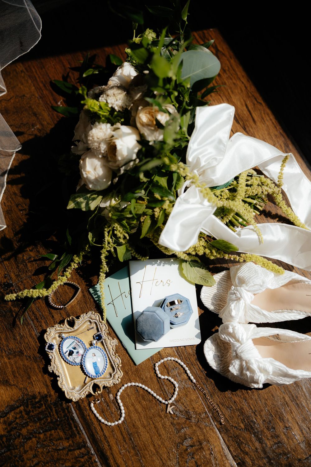 Wedding details flat lay with flowers, shoes, jewelry and photos on wooden surface.