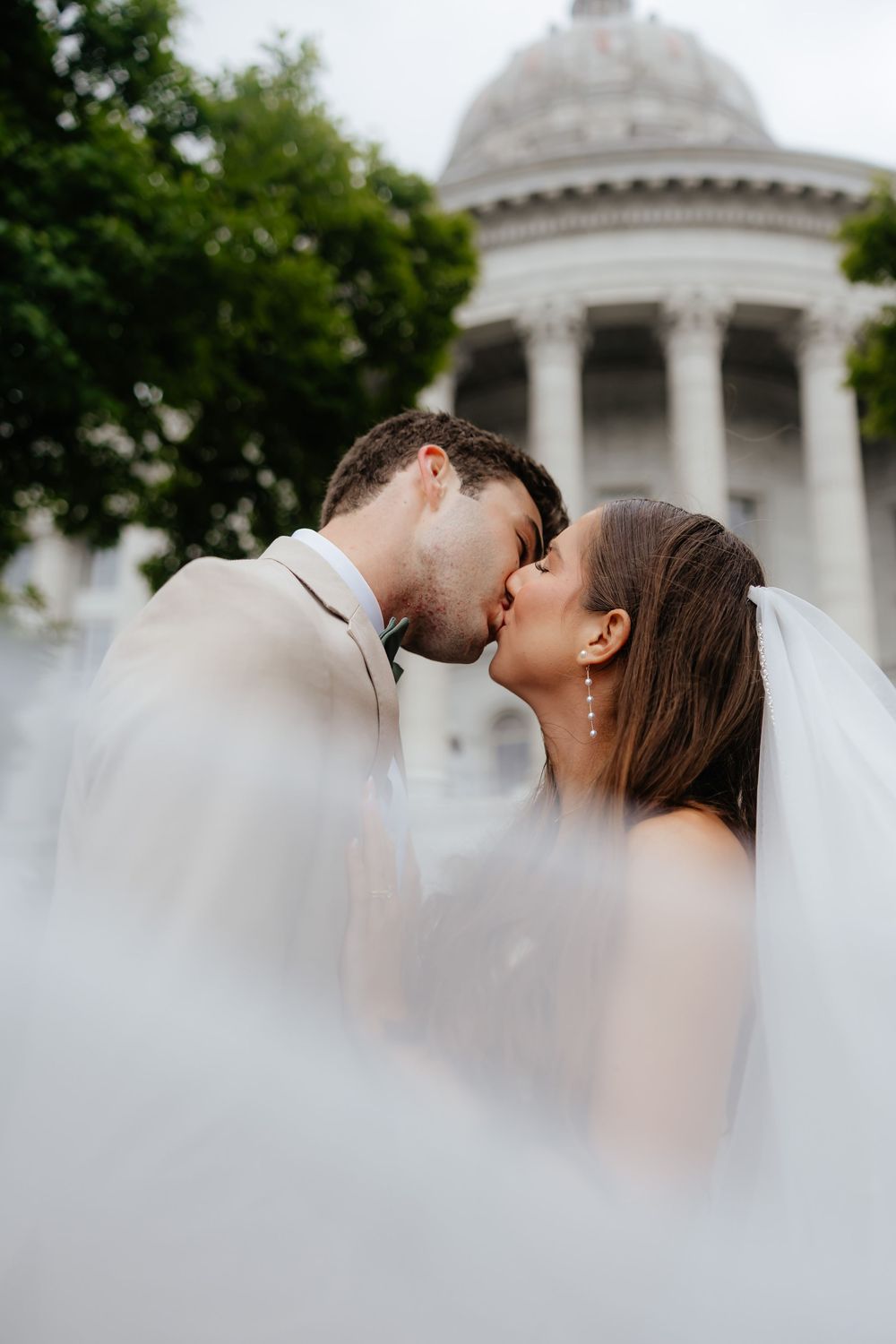 Romantic moment captured through soft veil with domed building in background.