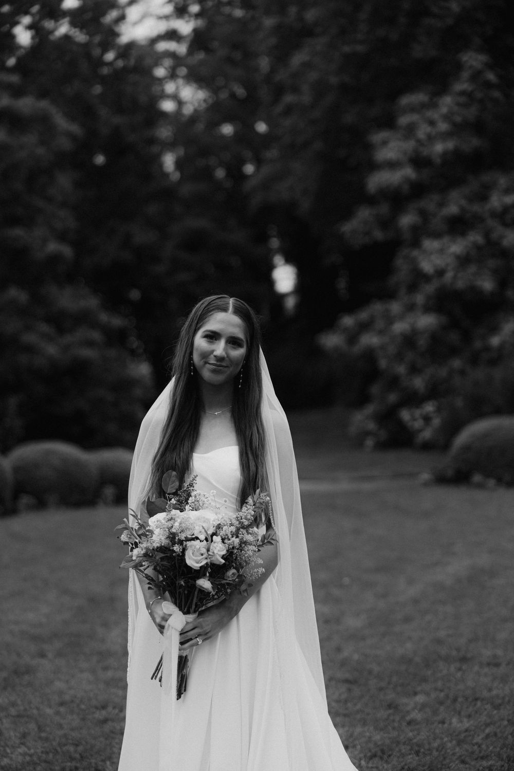 Black and white portrait of bride holding bouquet in garden setting.