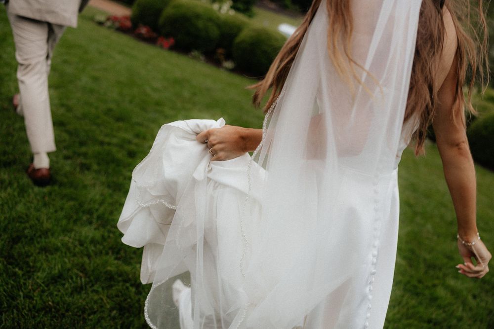 Flowing white wedding dress detail against green garden background.