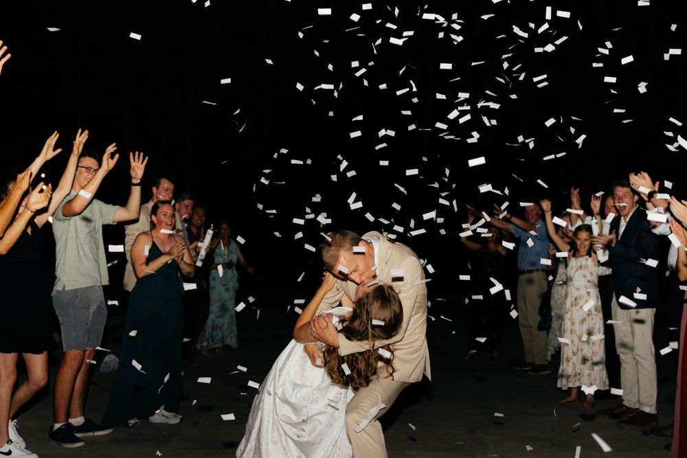 Wedding guests celebrate and dance joyfully at a nighttime reception with confetti falling from above.