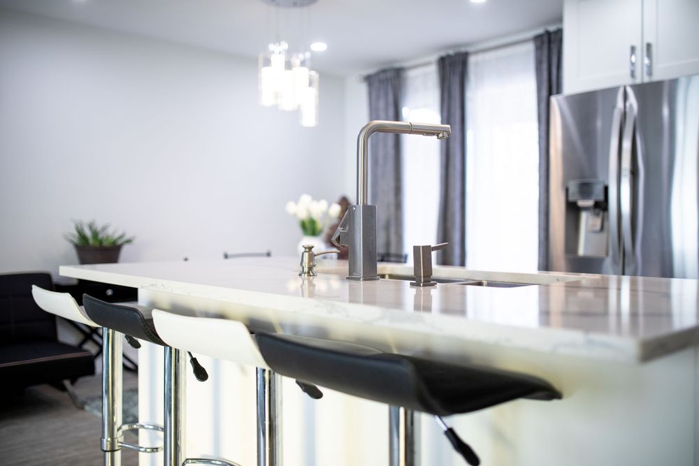 Modern white marble kitchen island with black bar stools and stainless steel appliances.