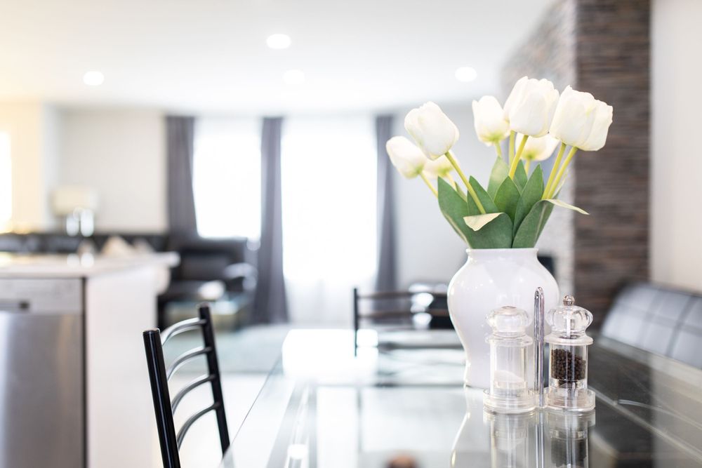 White tulips in a vase on a glass dining table in a bright modern open-concept living and dining room.
