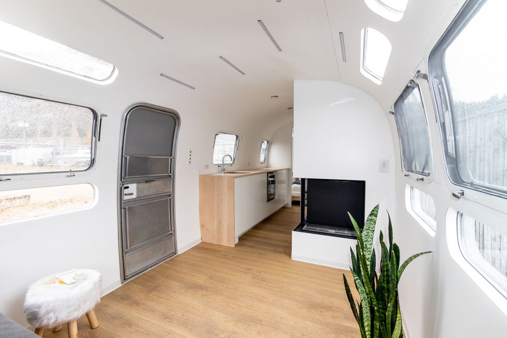 Minimalist white Airstream interior with light wood floors, built-in fireplace, and large windows.