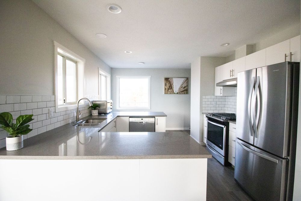Contemporary white kitchen with gray countertops, subway tile backsplash, and stainless steel appliances.