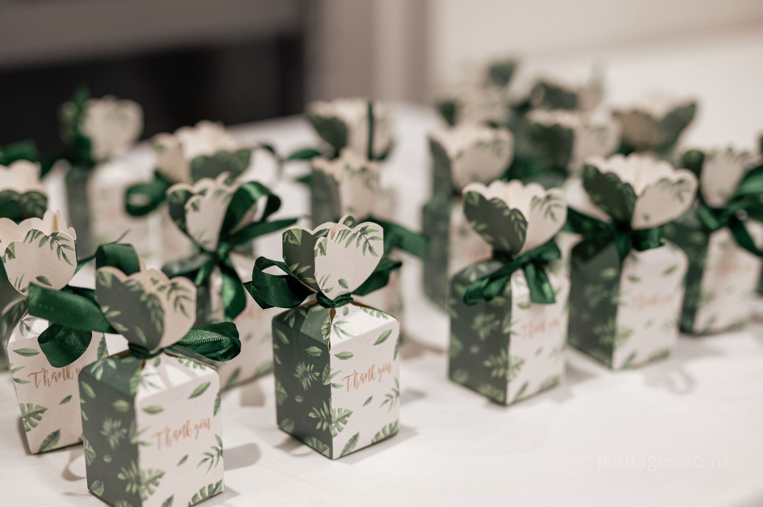 Wedding favor boxes with white floral designs and green ribbons arranged in neat rows for a special occasion.