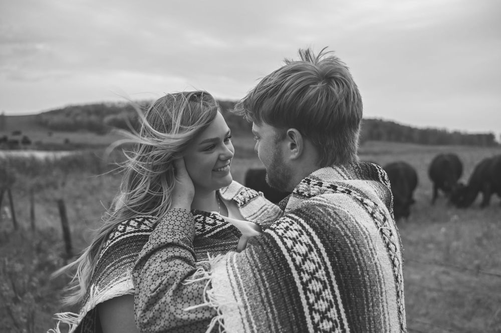A romantic black and white photo series showing a couple embracing in a rustic outdoor setting with mountains and fields.