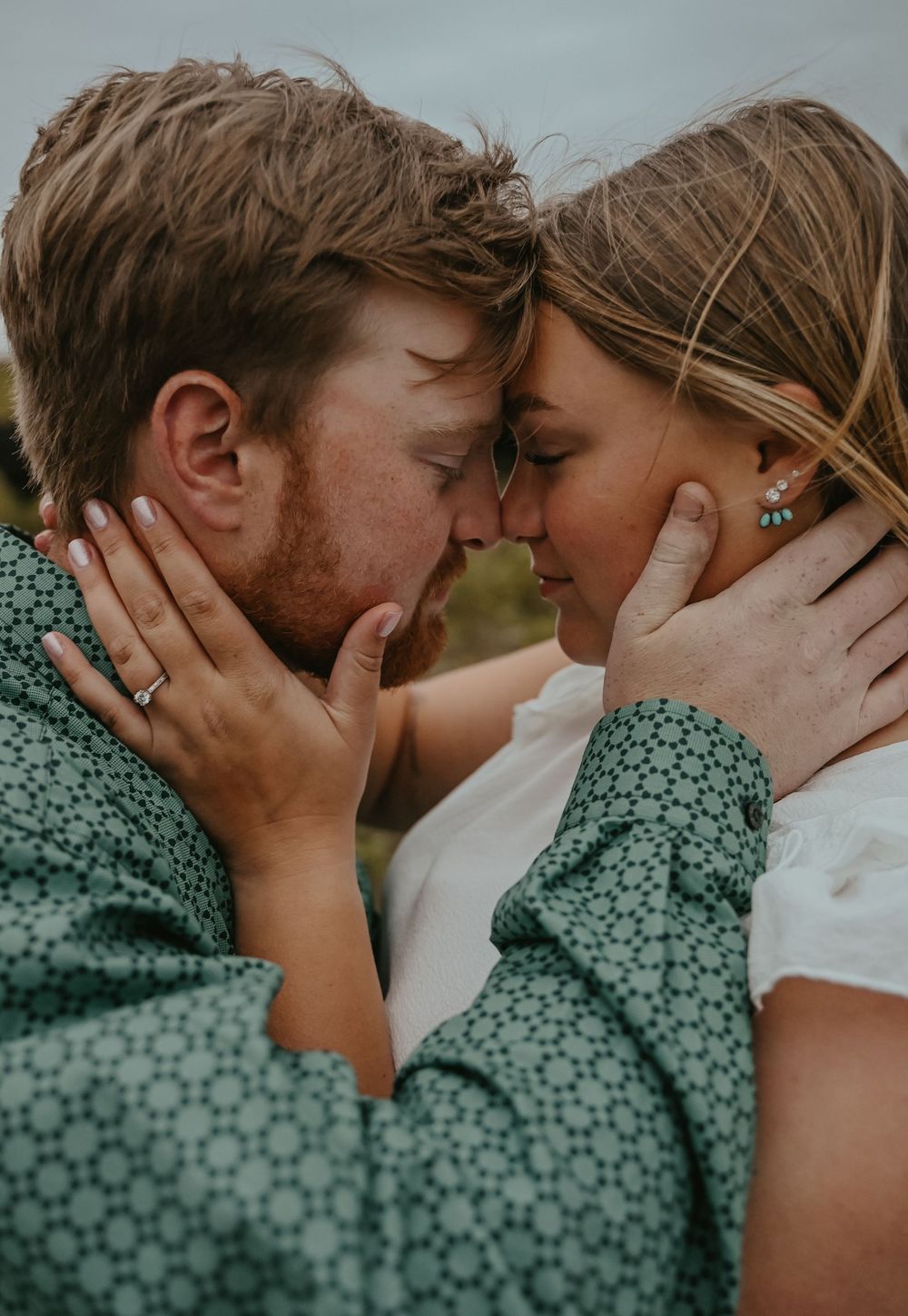 A tender intimate moment between a couple in matching green and white outfits against a natural backdrop.