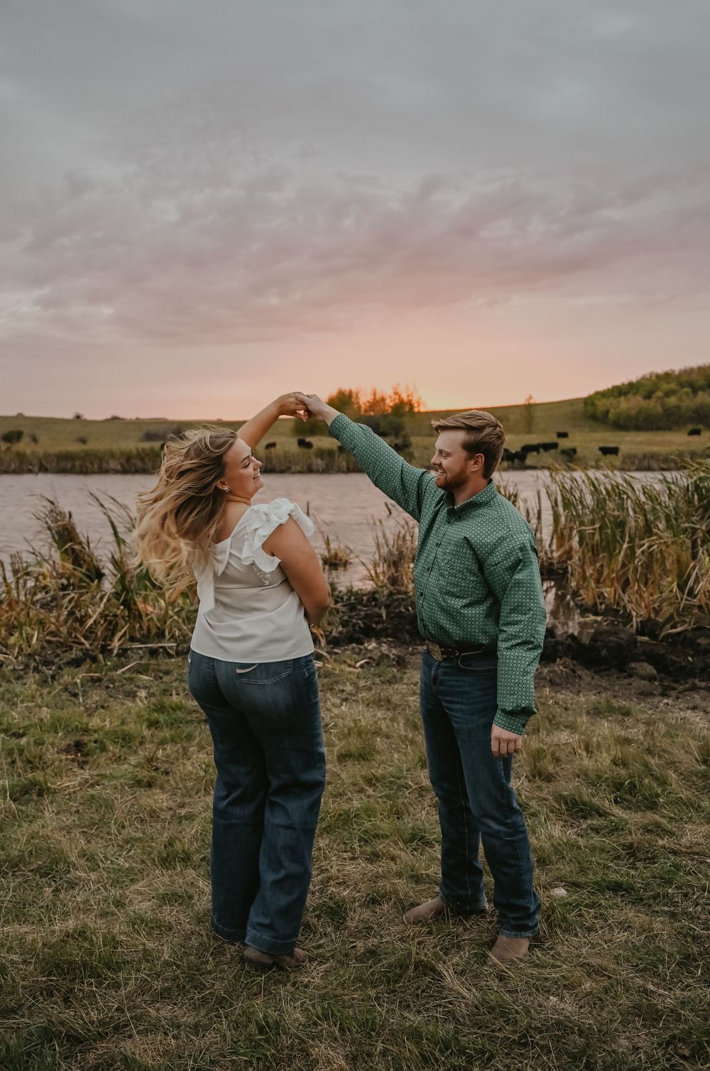 A playful couple enjoys a candid moment together in a grassy field during golden hour.