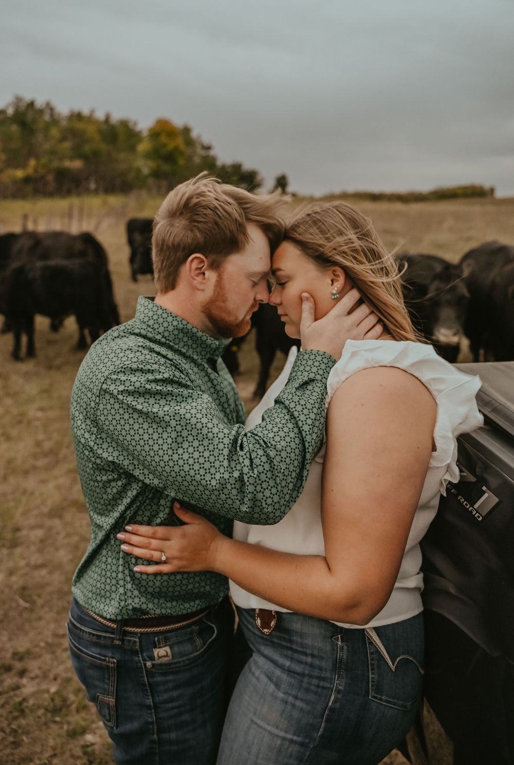 A romantic couple in matching green and denim outfits share intimate moments by a rustic fence at sunset.