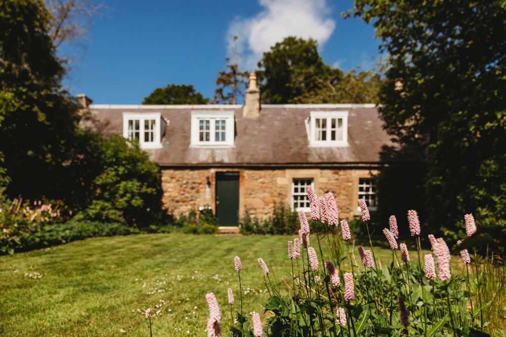 A panoramic view of multiple stone buildings and gardens in a countryside setting with blooming pink flowers.
