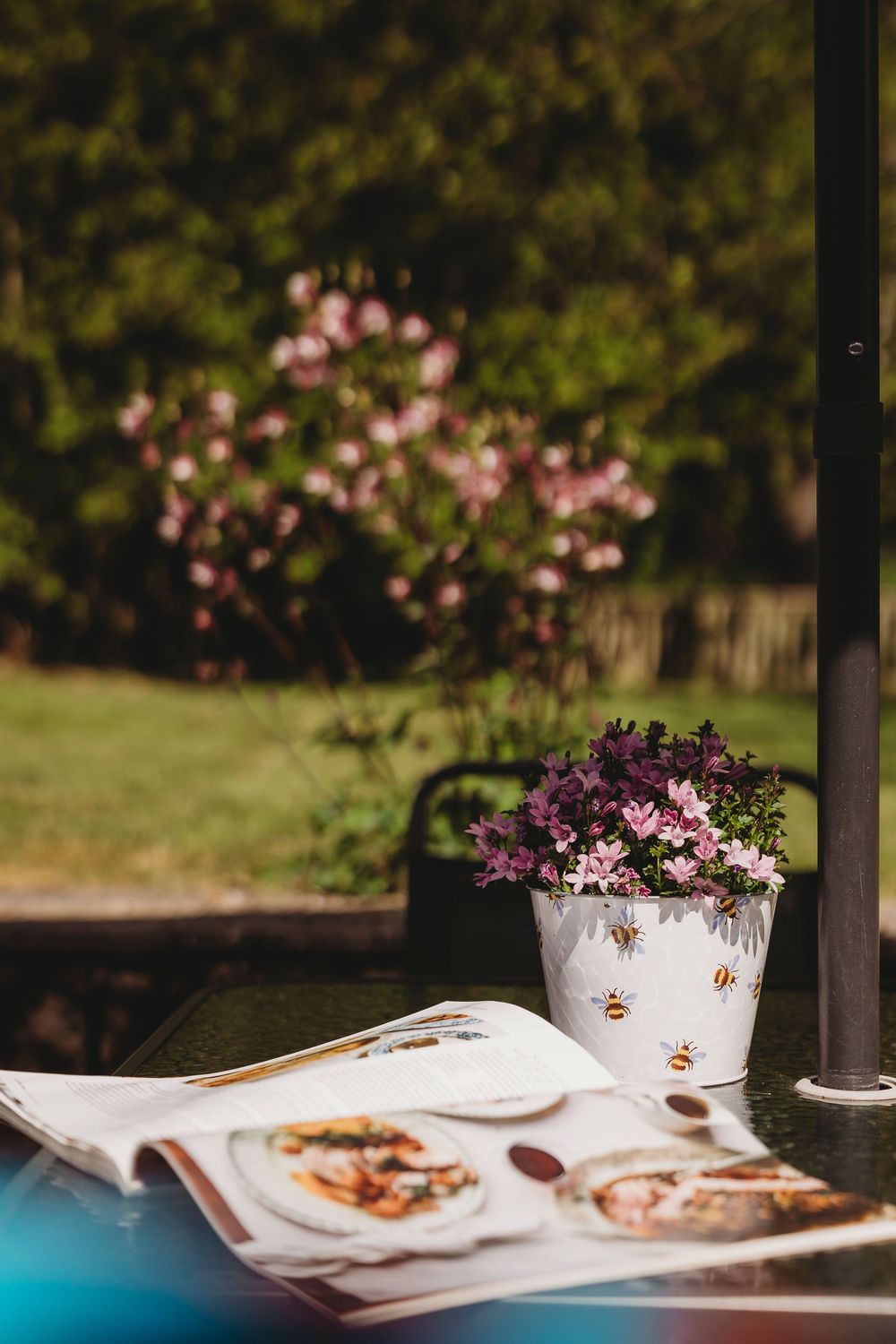Pink flowers in a decorative pot next to plates on an outdoor table setting.