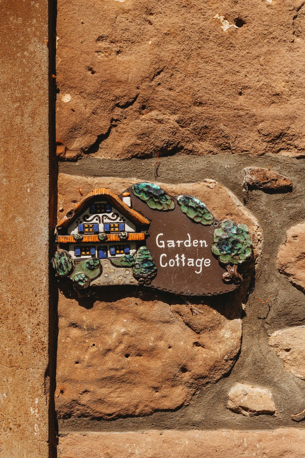 Three decorative wooden signs mounted on stone wall with text 'Cottage' and 'Garden' painted in rustic style.