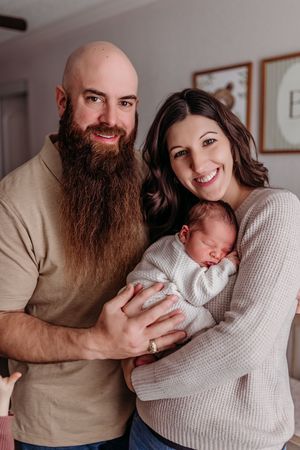 Happy couple smiling and holding their sleeping newborn baby wrapped in white during an in-home newborn photo session.
