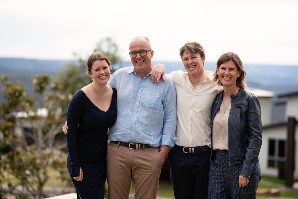 of four people standing outdoors, smiling the camera. The group consists of two women and two men. The man in the center is wear light shirt