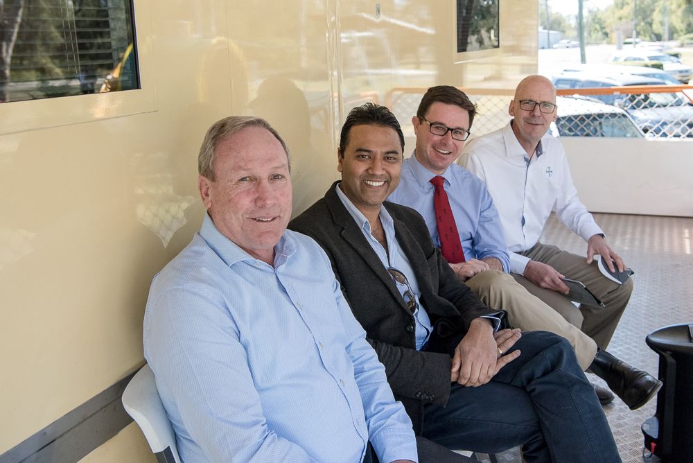 Four men are sitting on a bench outdoors They are dressed in business attire, with three wearing shirts and one in a suit jacket They appear