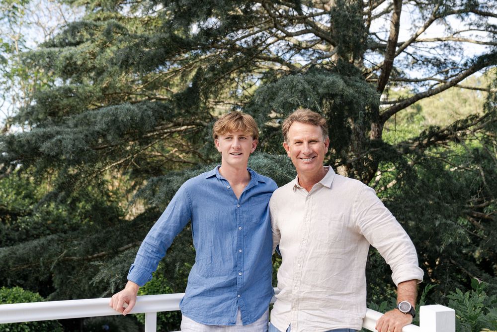 The shows people standing outdoors in front of a tree. They are both smiling, and have their arms around each other's shoulders. color shirt