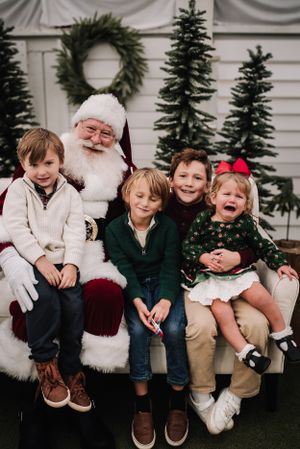 Holiday portrait with Santa Claus and children in front of decorated Christmas scene. Nashville family photographer specializing in natural