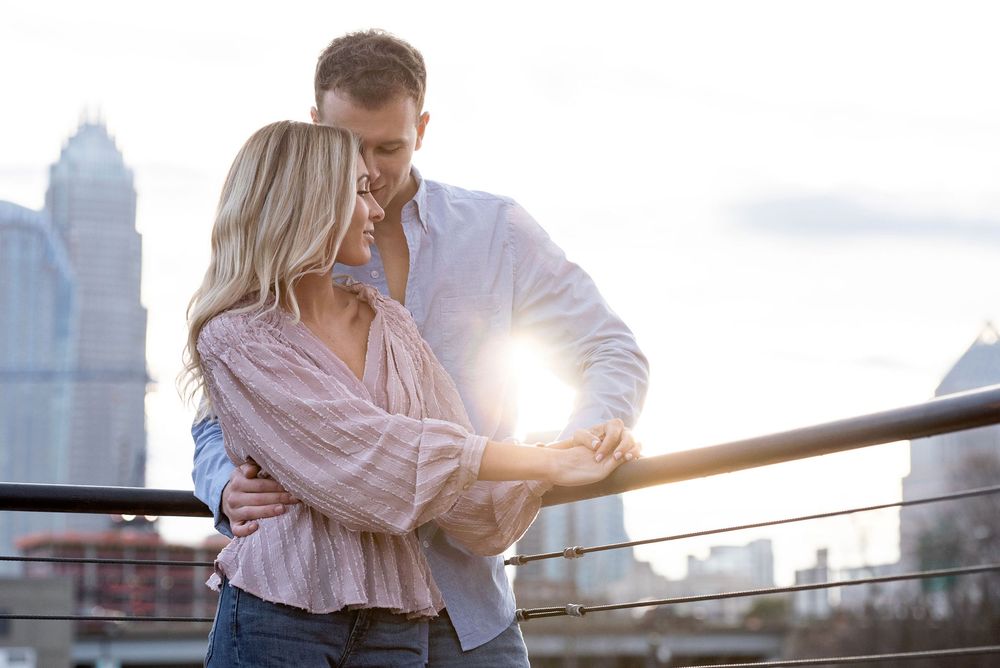 Romantic couple embracing at sunset with city skyline in background.
