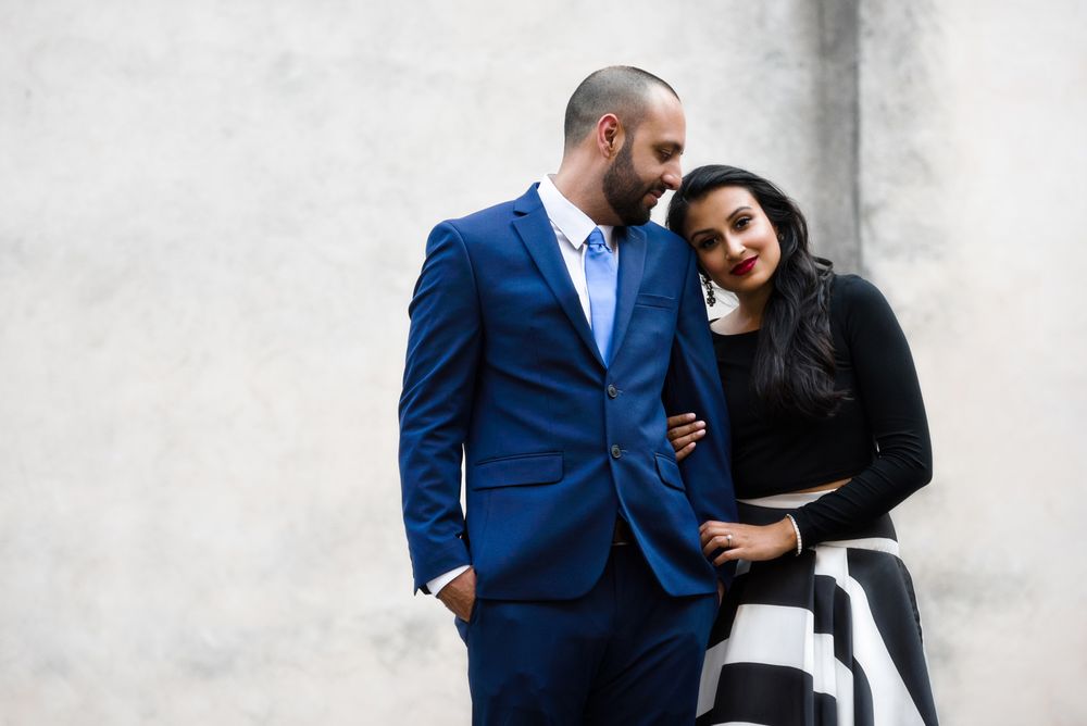 Stylish couple in formal attire posing against white wall.