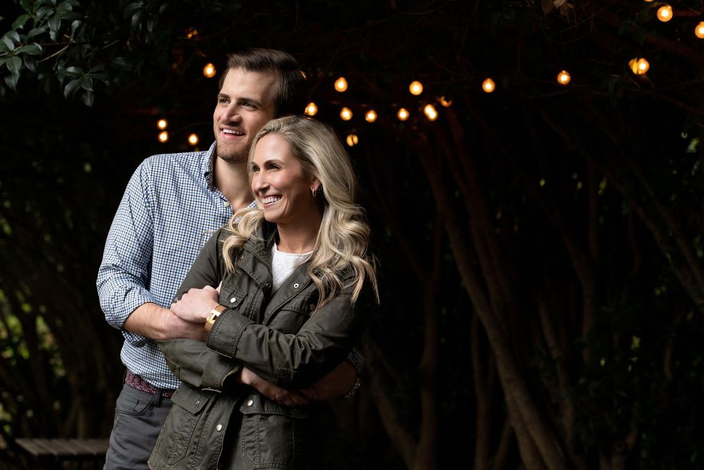Romantic evening engagement photos with string lights creating bokeh effect in background.