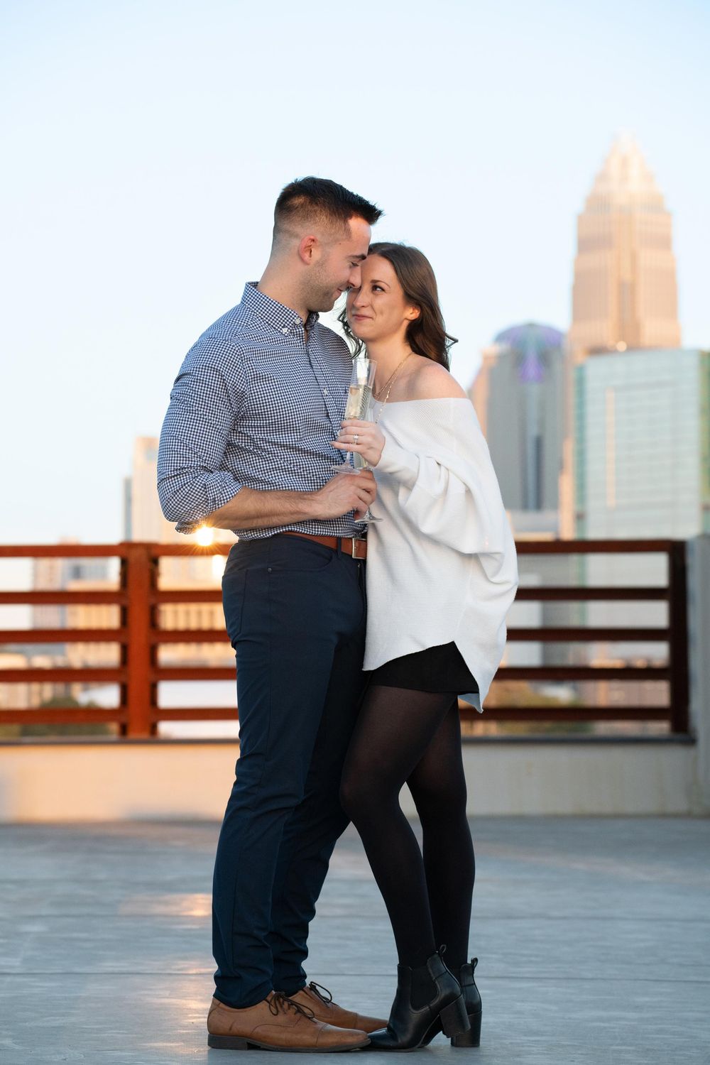 A couple shares a romantic moment during sunset on a rooftop overlooking a city skyline.