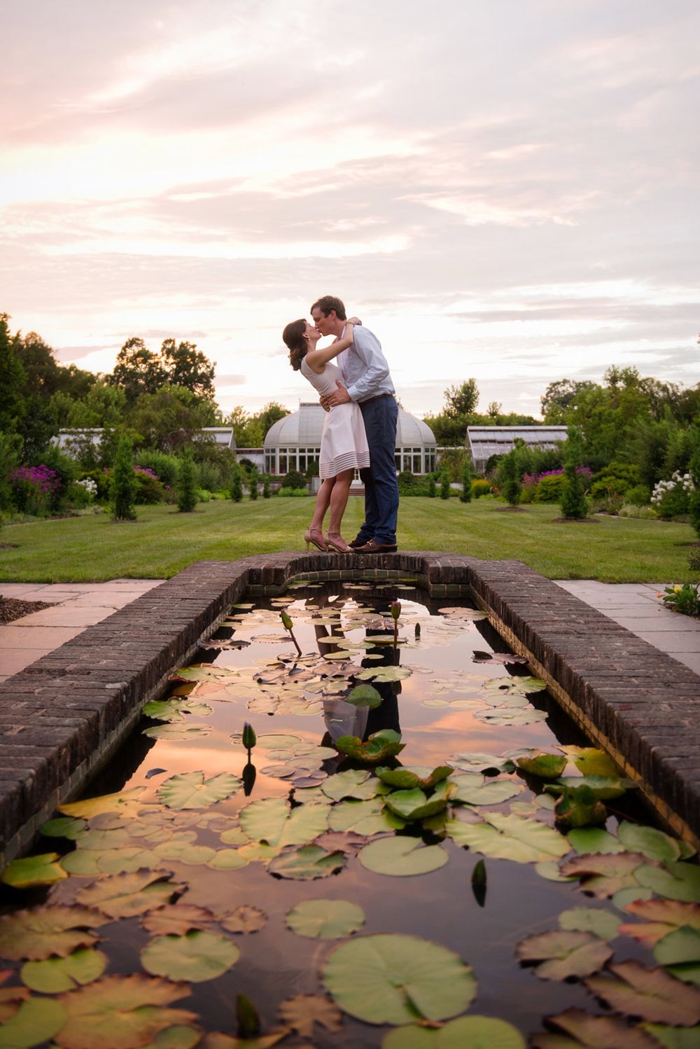 Couple sharing romantic moment on bridge over lily pond during sunset in garden setting.