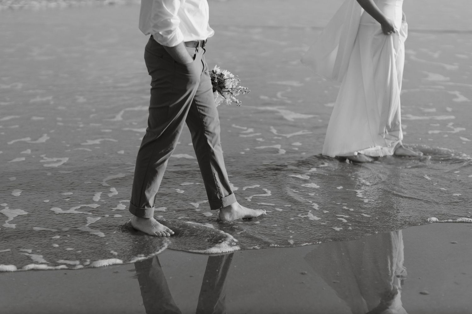 Black and white photo of couple walking through gentle ocean waves.