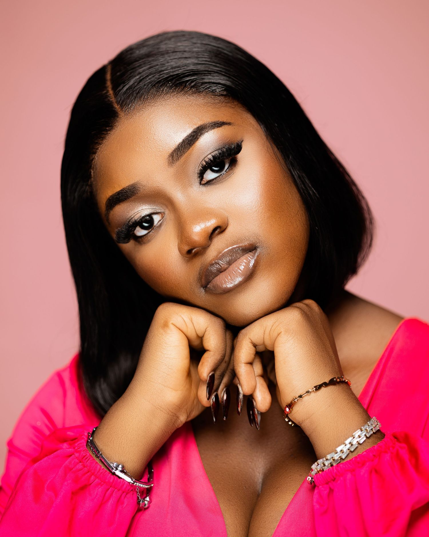 Studio portrait against pink background showcasing glamorous makeup and jewelry.