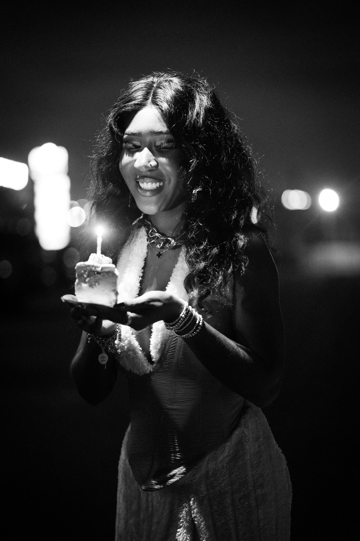 Black and white portrait of someone holding a lit birthday cake in evening wear.
