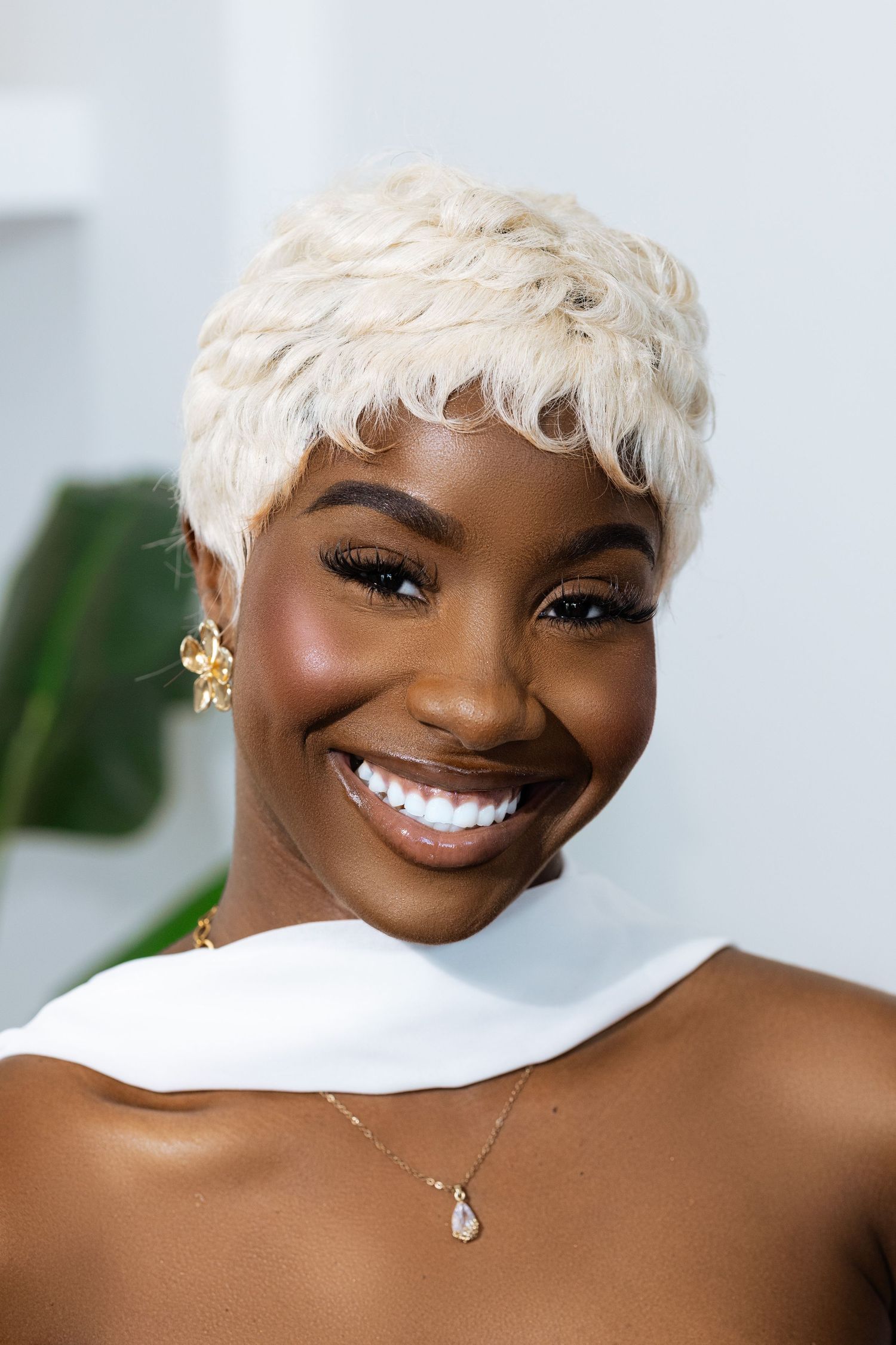 Close-up portrait with platinum blonde pixie cut and glamorous makeup against white background.