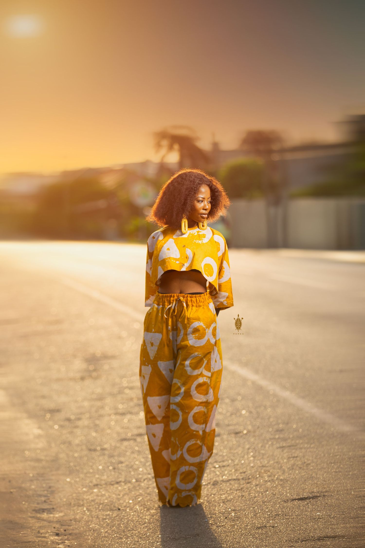 Figure in yellow patterned dress photographed during golden hour on empty road.