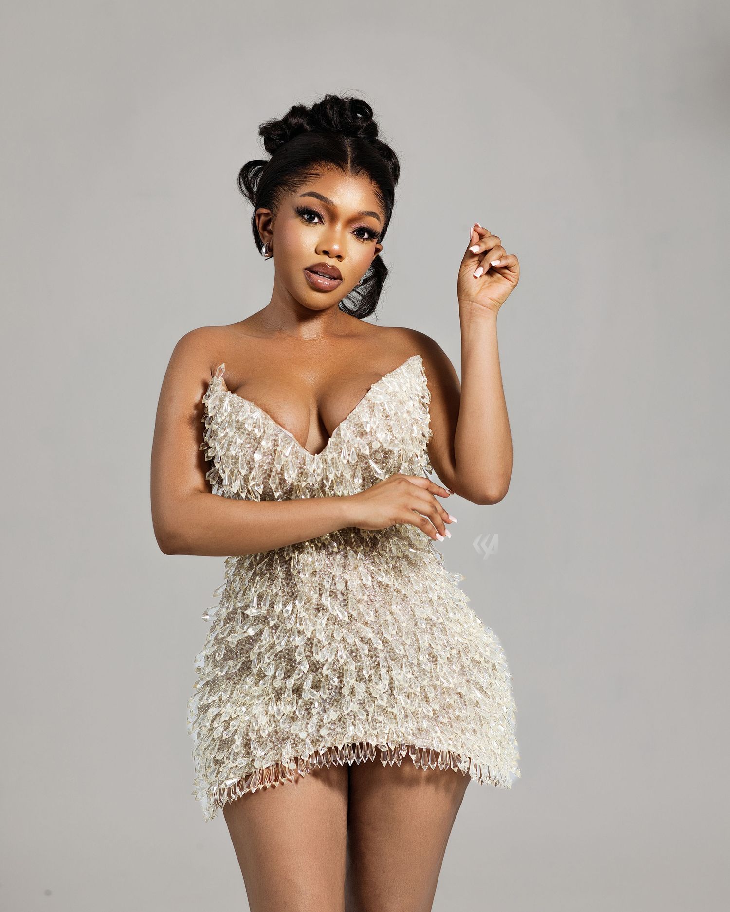 Woman in elegant cream feathered mini dress posing confidently against a neutral gray background.