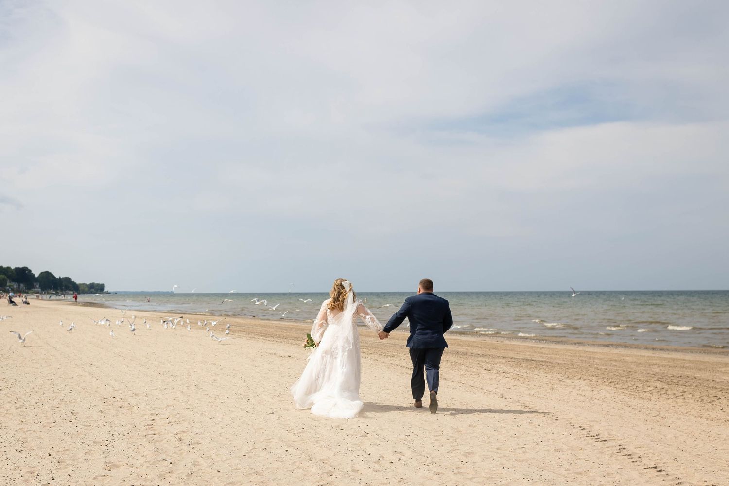 A wedding couple poses at a marina with sailboats and yachts in the background.