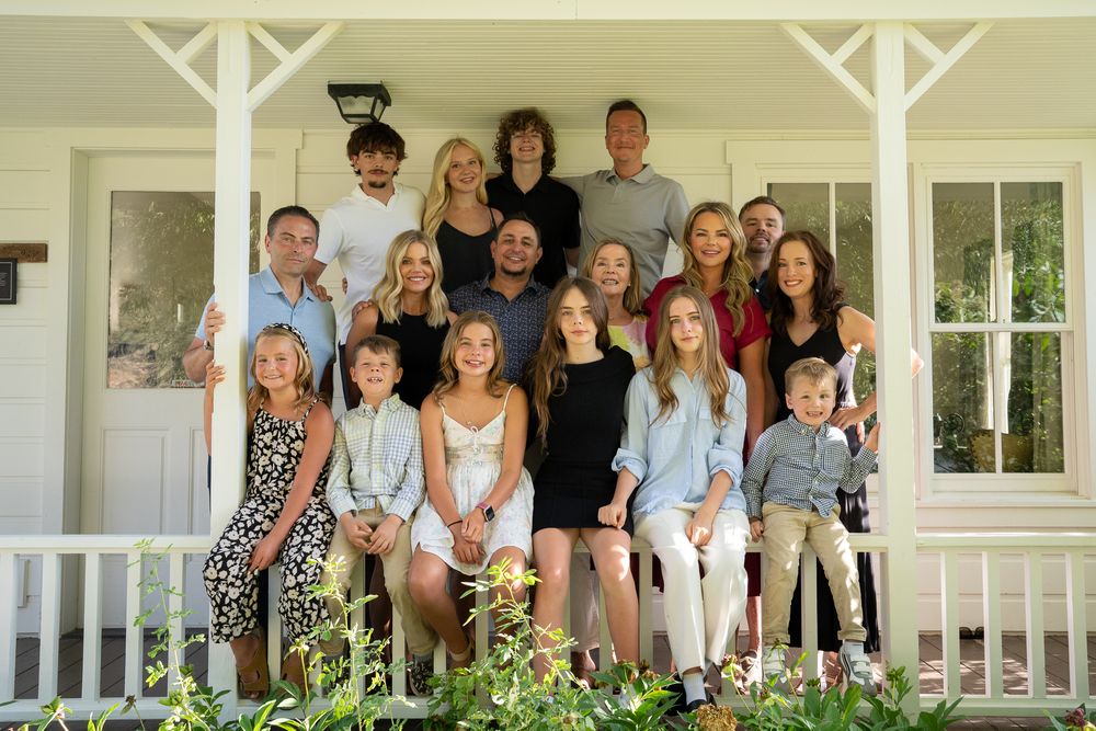 Smiling group of people standing together on a white front porch during a family gathering.