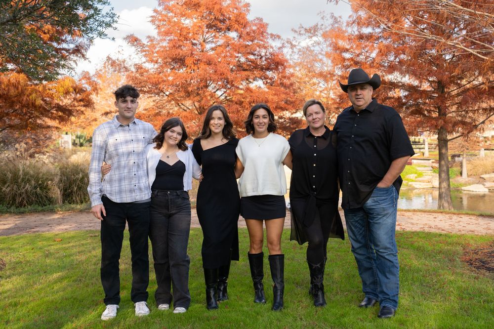 A group in black and casual attire poses together outdoors with vibrant orange autumn trees in the background.